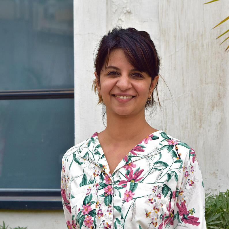 Shakun from chest up with straight dark hair, bangs, hair pulled back and wearing a floral top