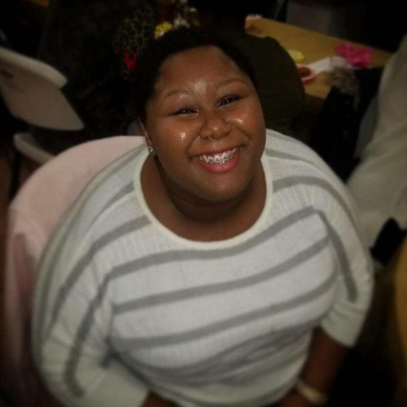 Mishael with a top angle showing an adorable smile with braces wearing white long sleeves shirt with light grey stripes