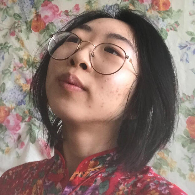 Liu from the shoulders up in a red floral top, dark straight shoulder length hair, wire glasses, and looking up to the left