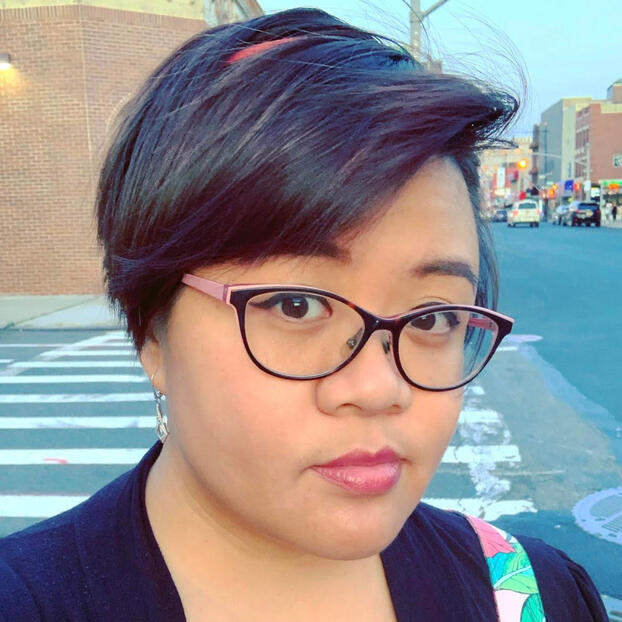 Caroline from shoulders up with dark brown straight hair and black/pink glasses